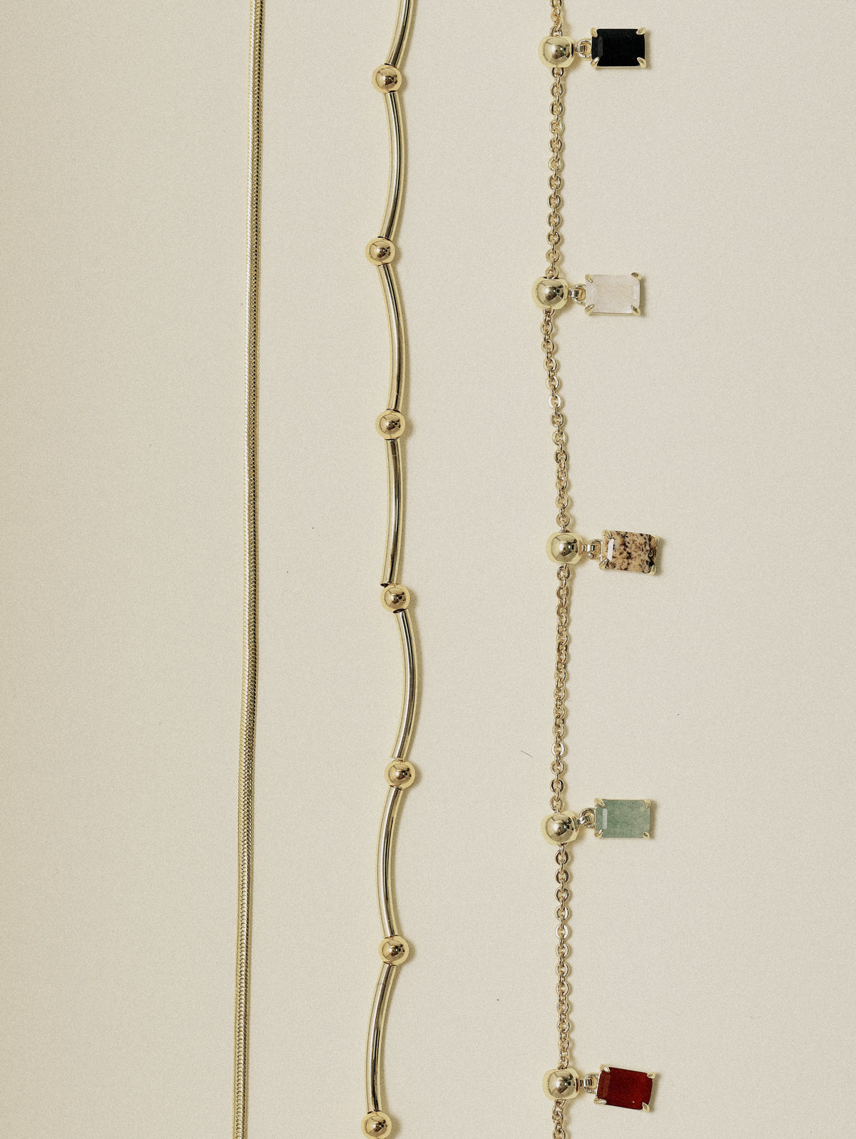 Detail of the Terre Snake Chain lying beside a charm chain, showing the flat liquid links