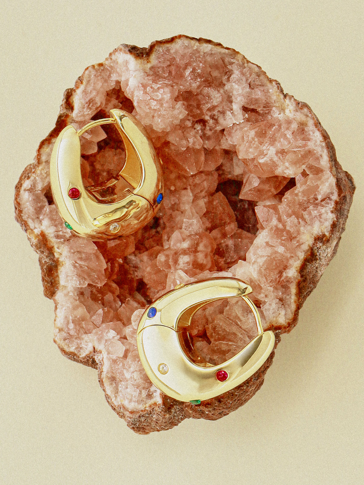 Two Terre Halo Hoops resting on a rough pink rose quartz geode, the tiny set stones catching the light
