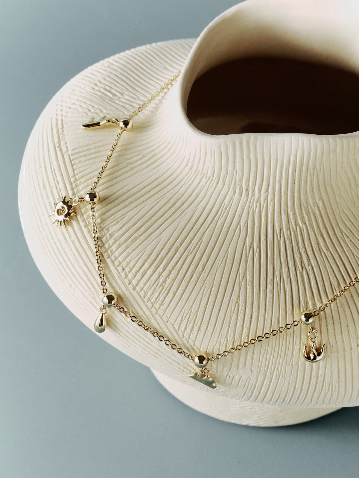 The Talisman Charm Necklace draped over a white ribbed ceramic form, the charms hanging free